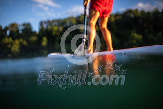 Young man on a paddle board. Getting a great exercise on a lovely river in warm evening sunlight - paddle underwater image