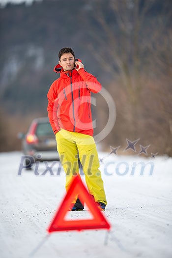 Young man calling car assistance service after his car has broken down on a cold winter day