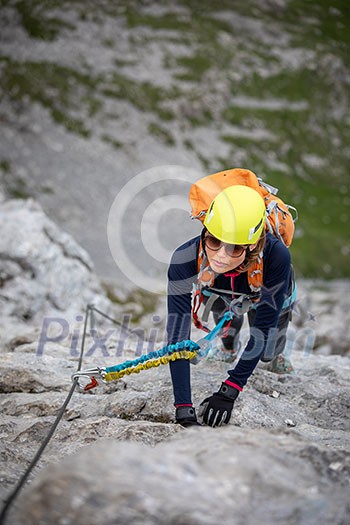 Pretty, female climber on a via ferrata - climbing on a rock in Swiss Alps