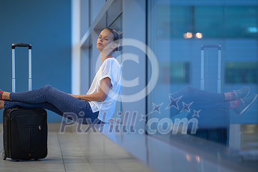 Exhausted female passenger waiting for her re-scheduled/delayed flight with her luggage at an international airport