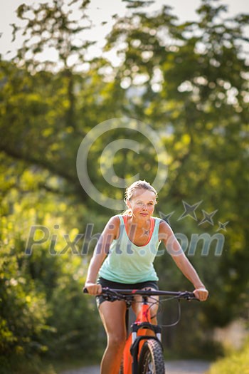 Pretty, young woman biking on a mountain bike enjoying healthy active lifestyle outdoors in summer (shallow DOF)