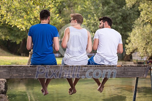 group of young men enjoying watermelon while sitting on the wooden bridge over the river in beautiful nature