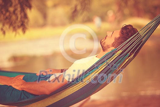 Young man resting on hammock while enjoying nature on the river bank Young man resting on hammock while enjoying nature on the river bank