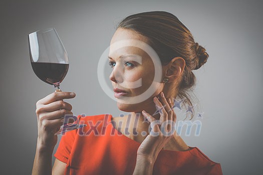 Elegant young woman in a red dress, having a glass of red wine