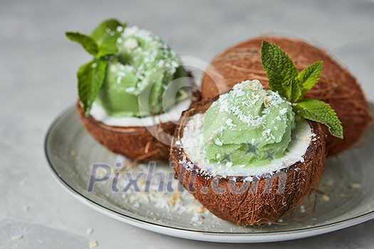 Tasty fresh green fruit sorbet in coconut peel with whole fresh coconut on gray background. Summer dessert. Soft focus.