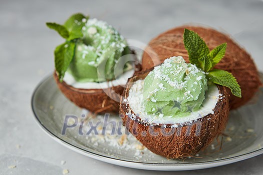 Tasty fresh green fruit sorbet in coconut peel with whole fresh coconut on gray background. Summer dessert. Soft focus. Tasty fresh green fruit sorbet in coconut peel with whole fresh coconut on gray background. Summer dessert. Soft focus.