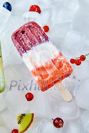 Creamy fruit colored ice cream lolly with different berries and slices of watermelon on ice cubes. Summer dietary cold dessert. Flat lay