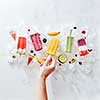 A set of different frozen berry smoothies lolly on a stick with years and fruits. The girl's hand takes a smoothie on a stick from ice cubes. Flat lay