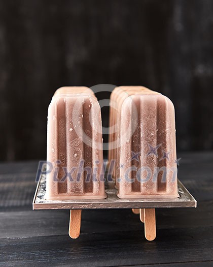 Natural chocolate ice cream popsicle in plastic forms presented on a black wooden table with a copy of the space for text