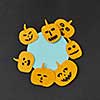 Creative card for invitation for Halloween with handmade paper round frame and yellow smiling scary pumpkins on a black paper, place under text. Flat lay