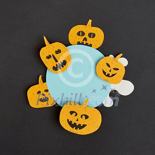 Decorative application handcraft from paper with terrible yellow pumpkins smiling on a blue round frame on a black background, place for text. Halloween concept. Flat lay.