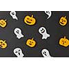 Decorative Halloween handcraft pattern from flying floating ghosts, spirits and smiling yellow pumpkins on a black paper background. Flat lay.