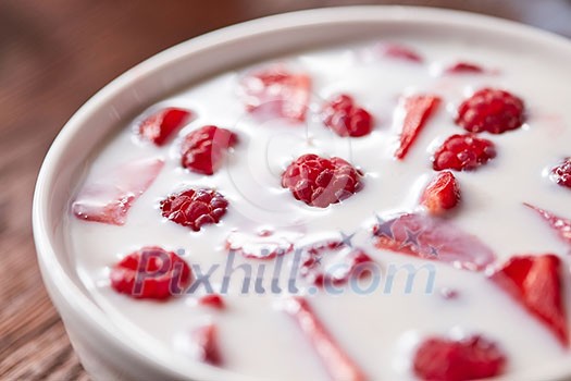Fresh delicious homemade breakfast of fresh yogurt with berries in a ceramic white bowl on a wooden background. Soft focus.