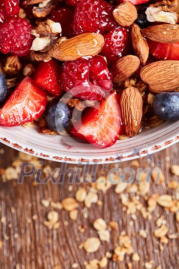 Dietary natural breakfast with fresh organic ingredients - berries, granola, nuts in a white bowl on a wooden table. Healthy vegetarian eating.