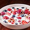 Preparing of natural breakfast with fresh organic ingredients - berries, granola, nuts, honey and pouring milk in a white bowl on a wooden table. Vegetarian detox eating