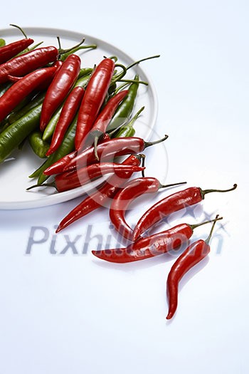 A composition of red and green chili peppers on a white plate isolated on a white background.