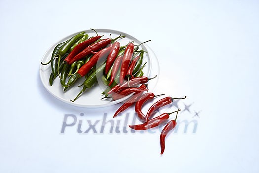 A composition of red and green chili peppers on a white plate isolated on a white background. A composition of red and green chili peppers on a white plate isolated on a white background.