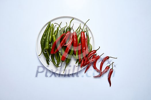 A composition of red and green chili peppers on a white plate isolated on a white background. Top view. A composition of red and green chili peppers on a white plate isolated on a white background. Top view.