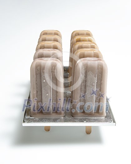 Homemade organic chocolate ice cream lolly in plastic molds with a reflection of shadows on a white background with copy space.