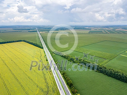 Aerial view of road through beautiful green field in the evening in summer. Beautiful landscape with speedway trees, green agricultural fields. Top view from flying drone.