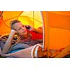 Pretty, young woman camping outdoors, lying in the tent in the morning, using her smart phone