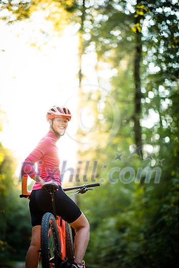 Pretty, young woman biking on a mountain bike enjoying healthy active lifestyle outdoors in summer (shallow DOF)