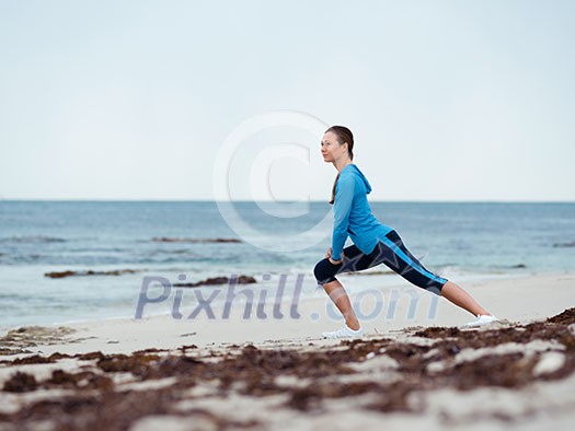 Sporty young woman stretching on the sea coast