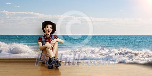 Smiling young beautiful woman sitting on the floor with ocean view. Mixed media