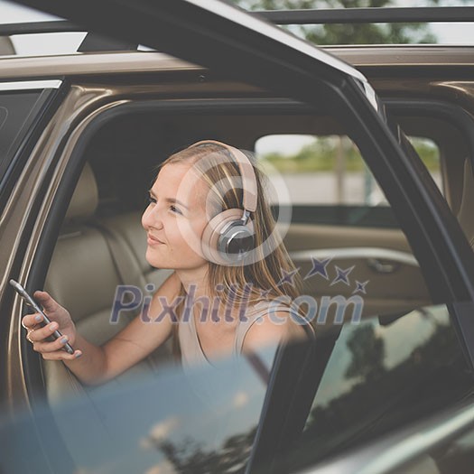 Cute teenage girl listening to her favorite music/audiobook on hig-end headphones during a roadtrip