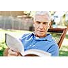 Handsome senior sitting in park and reading book