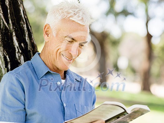 Handsome senior sitting in park and reading book
