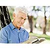 Handsome senior sitting in park and reading book