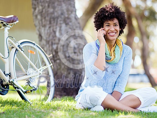 Charming young woman sitting in summer park and holding mobile phone