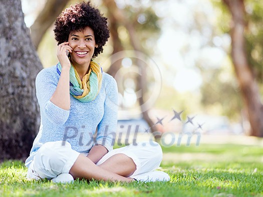 Charming young woman sitting in summer park and holding mobile phone