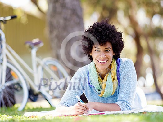 Beautiful young woman writing in her diary in summer park
