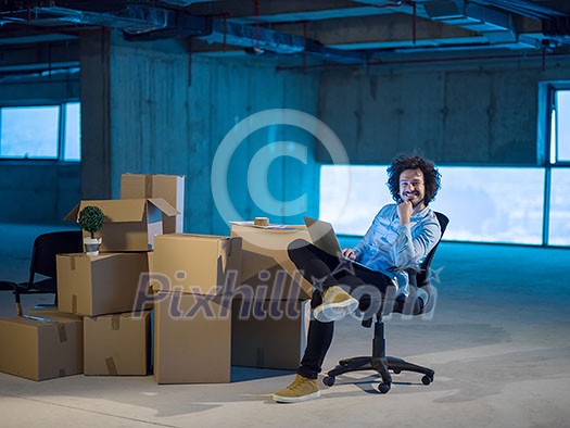 young male architect on construction site checking documents and business workflow using laptop computer with cardboard boxes around him in new startup office