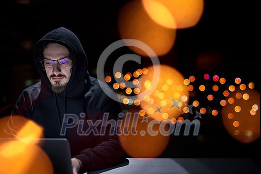 Young talented hacker using laptop computer while working in dark office with big city lights in the background at night