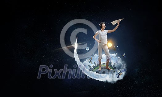 Joyful girl playing with paper airplane against the sky, standing on toy globe, dark space background