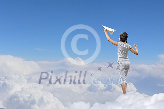 Back view of a girl playing with paper airplane against the sky, standing on clouds
