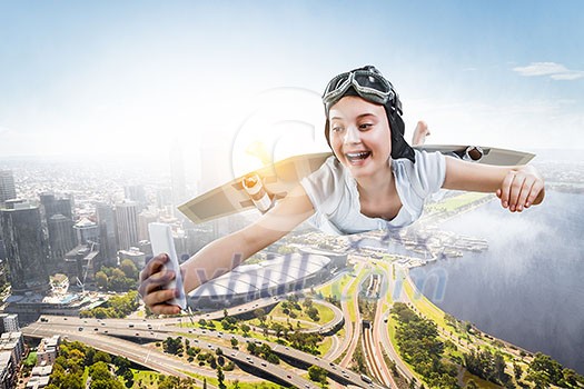 Joyful girl flying with self-made paper wing, making selfie, cityscape upper view