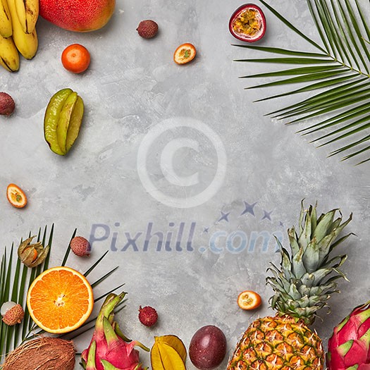 Various juicy exotic fruits, coconut, lychee, carom, pineapple and palm leaves on a gray concrete background with space for text. Food layout. Flat lay