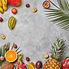 Various juicy exotic fruits, coconut, lychee, carom, pineapple and palm leaves on a gray concrete background with space for text. Food layout. Flat lay