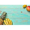 Corner frame of tropical fruits, banana, mango, carambola and pineapple on a blue wooden background with copy space. Flat lay
