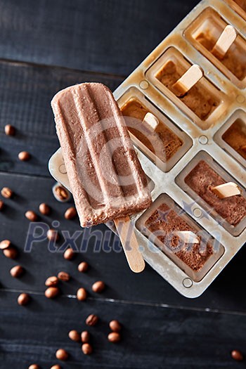 Homemade popsicles with chocolate on ice cube container with coffee beans on dark wooden background, flat lay. Homemade prepare concept