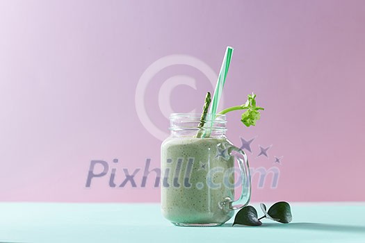 Vegetarian healthy smoothies from green vegetables with green leaves and plastic straw in a glass bowl on duotone pink green paper background.