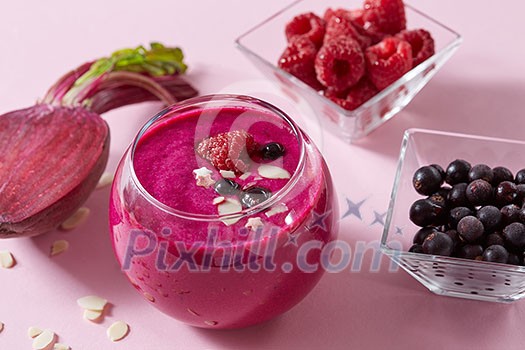 Vegetarian healthy smoothies from red berries and beetroot with almond plates in a glass cup on a pink paper background.