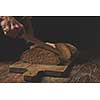 men's hands cut homemade a freshly baked dark bread on a wooden cutting board on the background of an old brown table