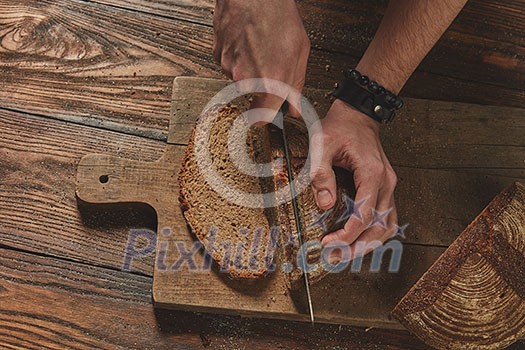top view of fresh bread cut into a man's hands on a wooden board.in the background of a brown table flat lay top view of fresh bread cut into a man's hands on a wooden board.in the background of a brown table flat lay