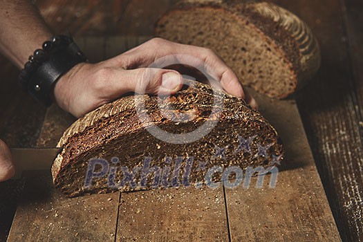 fresh organic bread on a wooden board cut into a man's hands. on a background of a brown table fresh organic bread on a wooden board cut into a man's hands. on a background of a brown table
