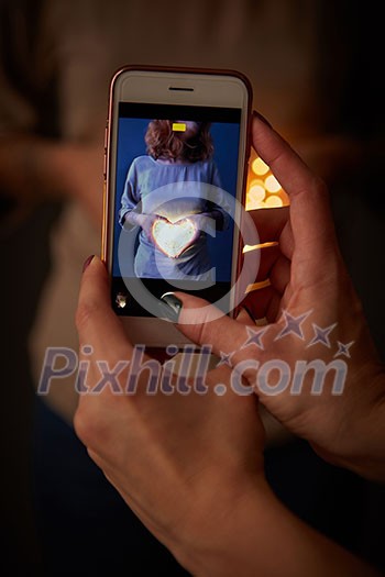 The phone with the image of a girl with a glowing heart is holding a woman in a blurred background with a beautiful bokeh. The phone with the image of a girl with a glowing heart is holding a woman in a blurred background with a beautiful bokeh.